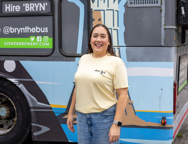 Woman standing in front of the Gower Brewery bus wearing yellow Gower Brewery T-shirt