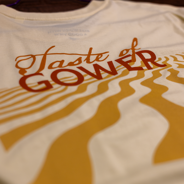 Closeup of a Gower Brewery T-shirt with 'Taste of Gower' text and sand design 