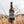 Load image into Gallery viewer, A person holding a bottle of Lighthouse Welsh Lager beer in a field with tall grasses.
